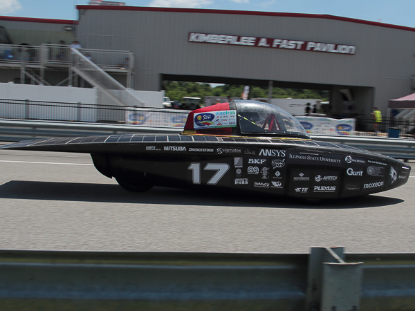 Solar-powered race car number 17 on a racetrack with a building in the background.