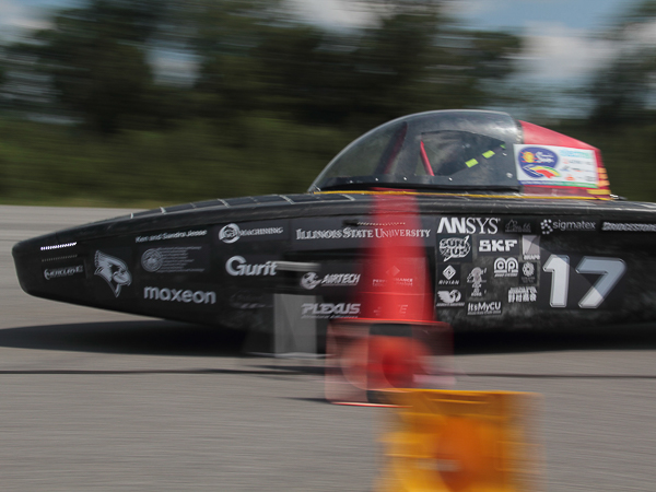 A black solar car with the number 17 races past a red traffic cone on a track.