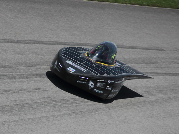 A solar-powered vehicle with a sleek design covered in solar panels, racing on a road.