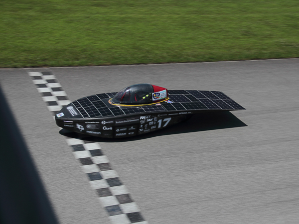 Solar-powered vehicle crossing a checkered finish line on a racetrack.