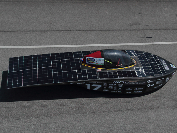 Solar-powered race car with a cockpit and solar panels on a road.